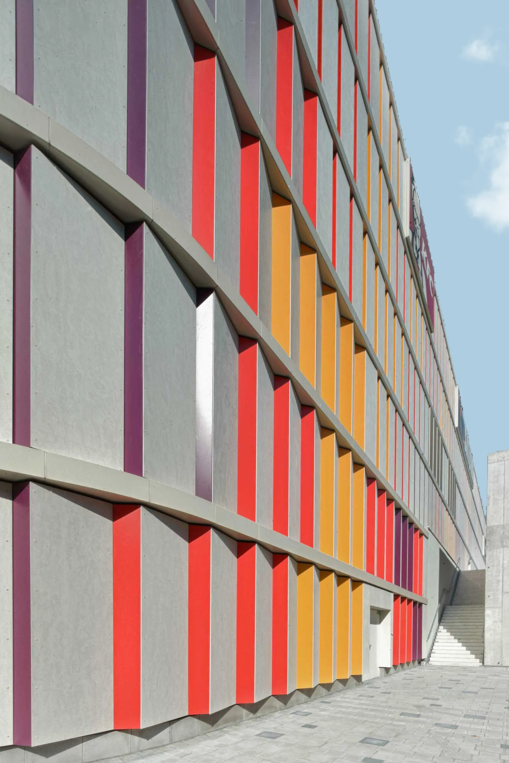 Fassadendetail mit vertikalen roten und orangefarbenen Sonnenschutzelementen