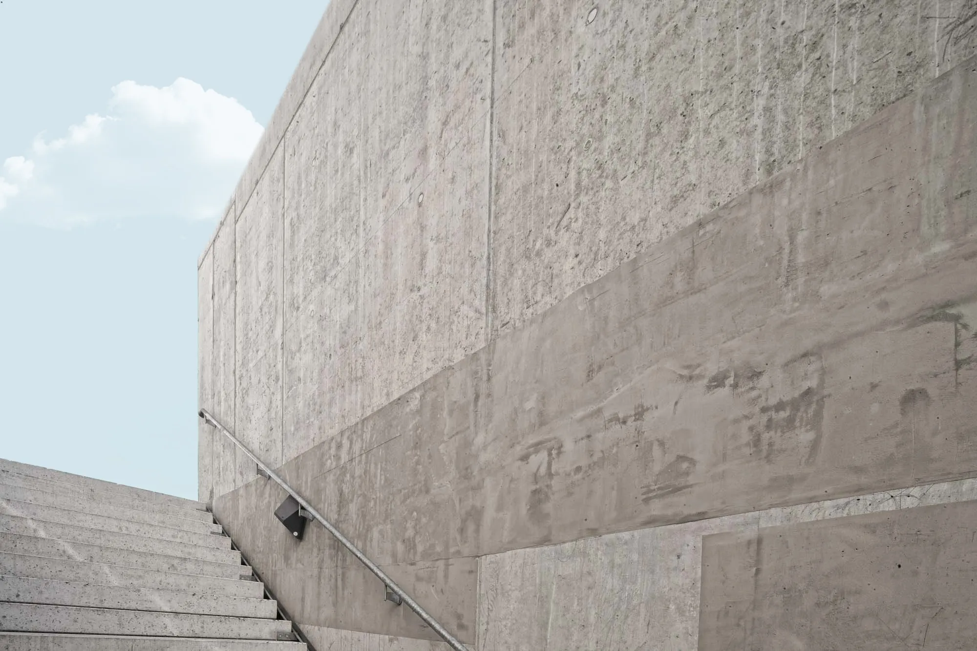 Betontreppe entlang einer hohen Sichtbetonwand unter blauem Himmel