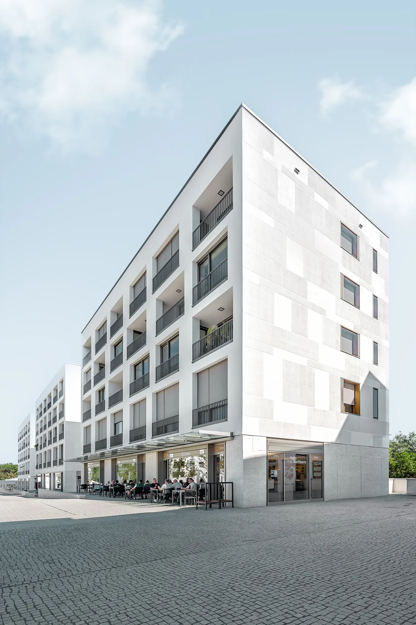 Weißes Eckgebäude mit tiefen Fensterlaibungen an einem gepflasterten Platz