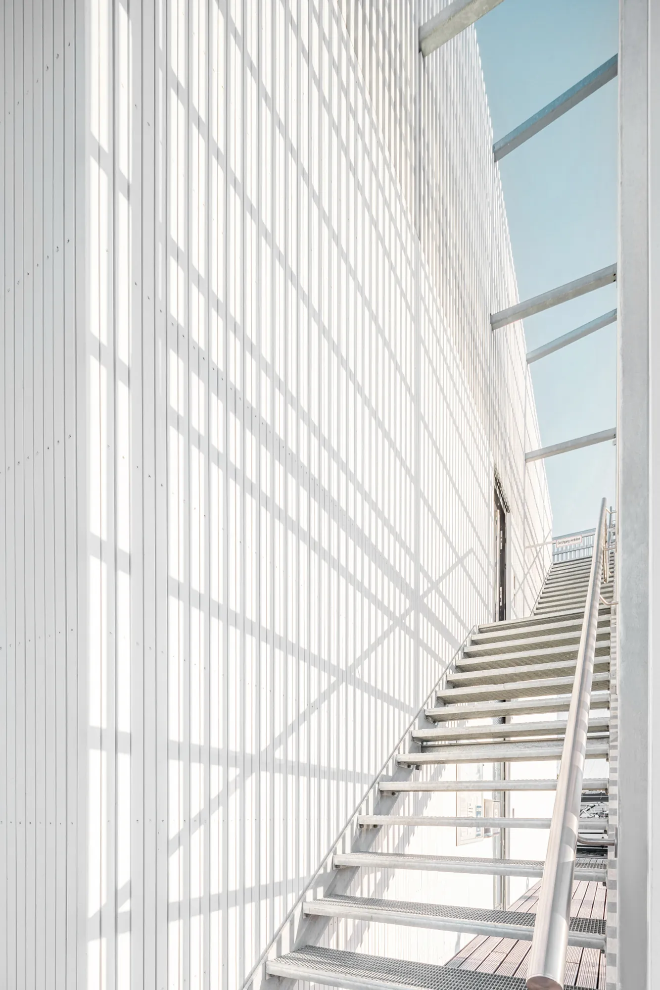 Weiße Treppe entlang einer hohen Glasfassade mit geometrischen Schatten