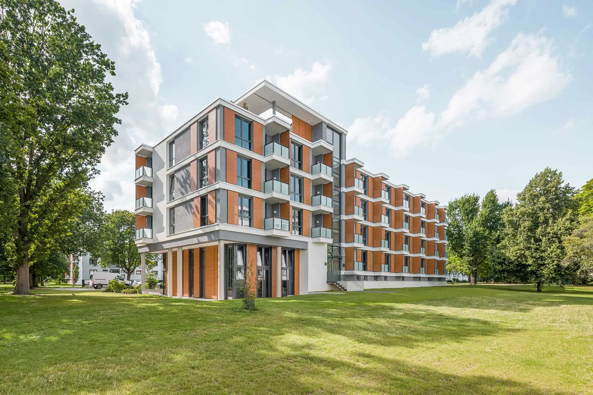 Mehrgeschossiges Gebäude mit Holzlamellen, Balkonen und vorgelagerter Grünfläche
