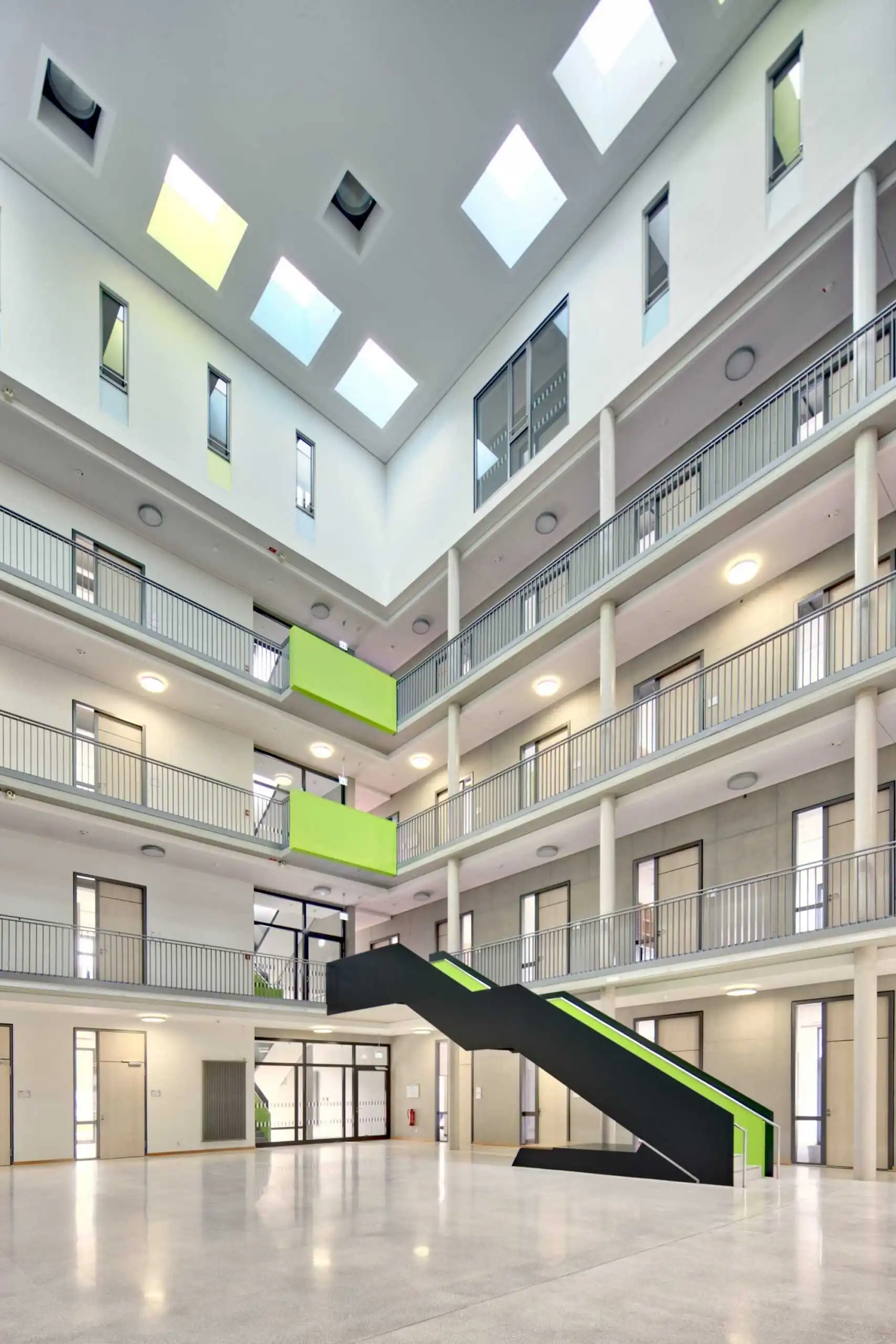 Mehrgeschossiges Atrium mit offenen Galerien, Treppe und grünen Akzenten