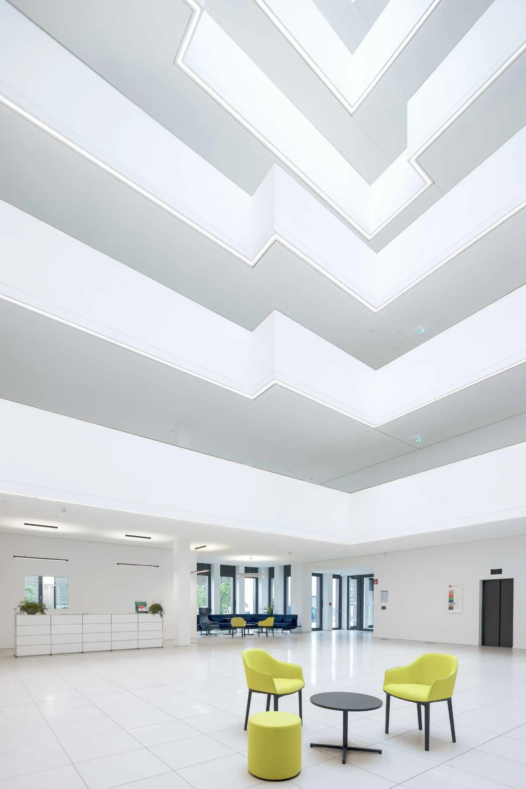 Atrium mit gestaffelten weißen Galerien und grünen Sitzmöbeln